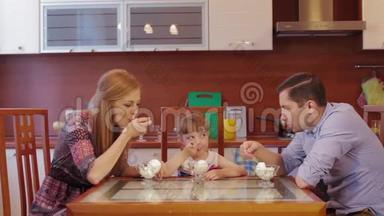 父母和女儿在家厨房吃冰淇淋。 可爱的小女孩在厨房的碗里吃冰淇淋